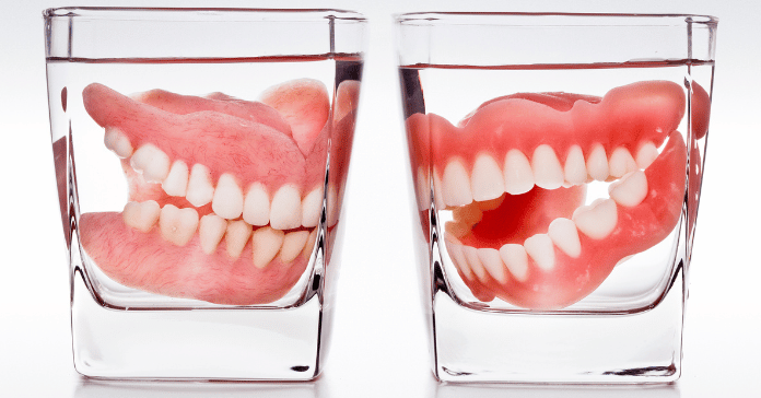 Full dentures soaking in clear water-filled glasses to keep them clean and moist.
