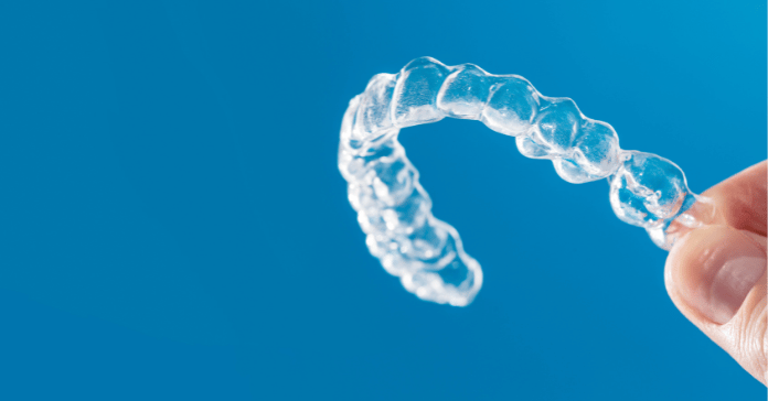 Hand holding an invisible clear aligner for teeth straightening.