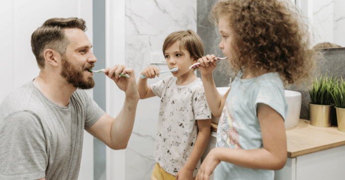 Father teaching his children how to brush their teeth properly using toothbrushes.