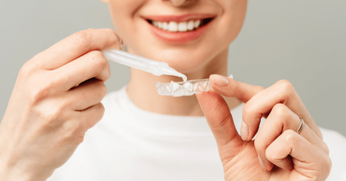 Smiling woman applying whitening gel to a clear dental tray for at-home teeth whitening.