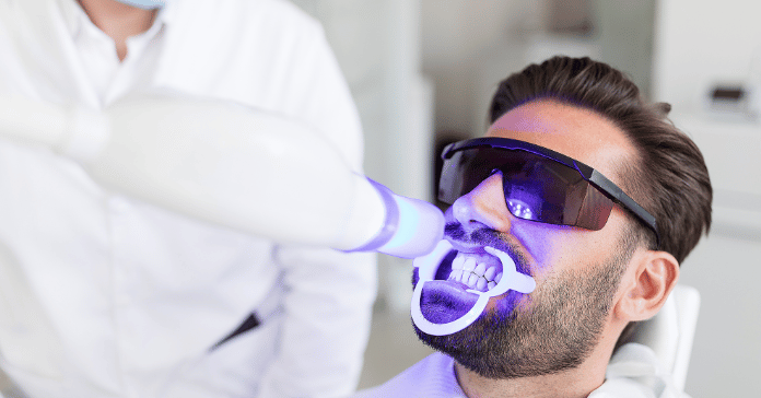 Dentist performing professional in-office teeth whitening using a blue LED light.