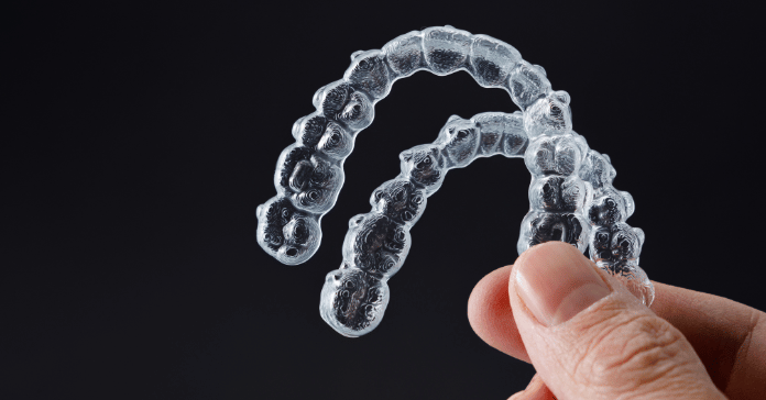 Clear aligners held in hand against a dark background.