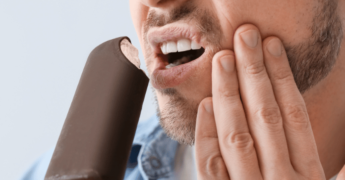 Man reacting with tooth pain while biting a cold ice cream bar due to teeth sensitive to cold.